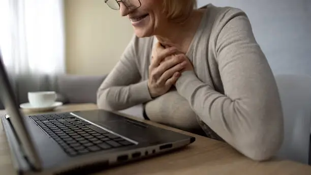 Old female delighted to talk to children in internet looking at laptop screen