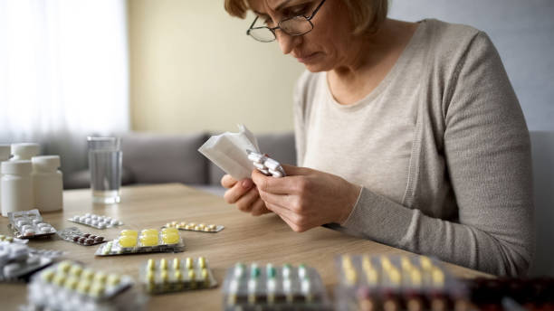 istock Sick elderly lady sitting at home table, reading pills instruction medicine 1048744600