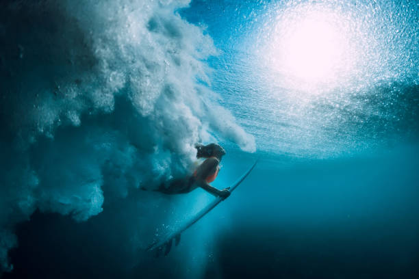 istock Surfer girl with surfboard dive underwater with under big ocean wave. 1048747246