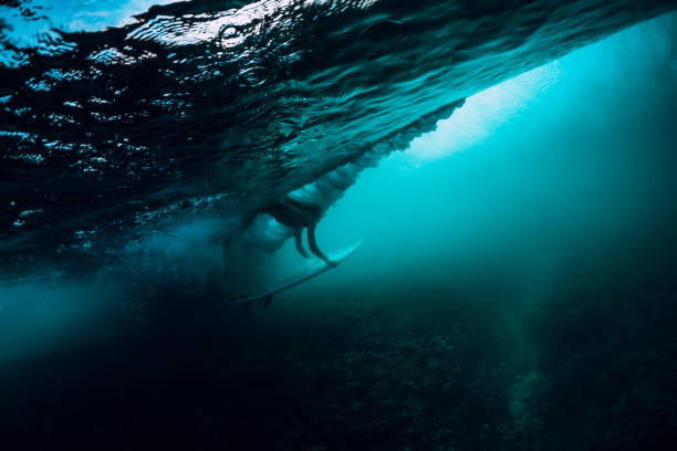 istock Alone surfer girl with surfboard make duck dive underwater with big ocean wave. 1048747312
