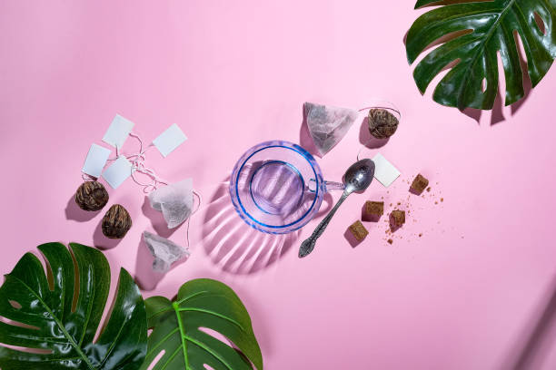 istock Workspace frame with green tropical leaf and tea cup, tea bag and sugar on pastel pink background with deep shadows. Flay lay. 1048748366