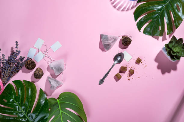 istock Workspace frame with green tropical leaf and tea cup, tea bag and sugar on pastel pink background with deep shadows. Flay lay. 1048752400