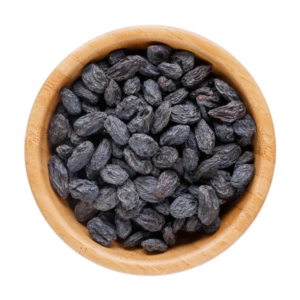 Black raisins in wooden bowl isolated on white. Dried fruits. Top view