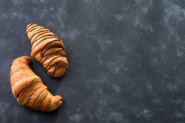 istock freshly baked croissant decorated with chocolate sauce isolated on a black slate background. Top view with copy space 1048756580