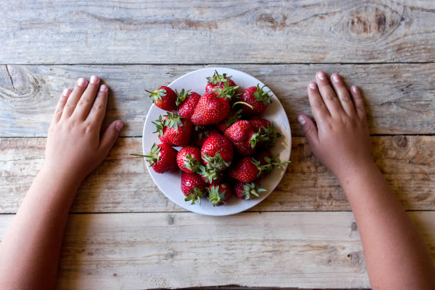 istock top view of a strawberry in a plate between children's hands on a table 1048761222