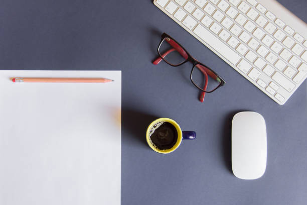 istock Blue desktop with blank sheet, pencil, cup of coffee, glasses, white mouse and white keyboard 1048771692