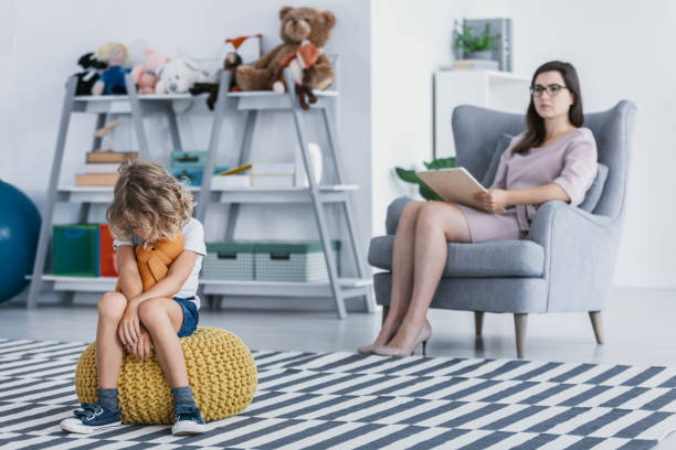istock A withdrawn child with an autism spectrum disorder sitting on a pouf during an evaluation session with a professional therapist in an office. 1048781744