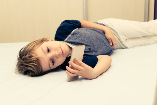 Cute Boy Watching Cartoons Online While Lying Down On Bed Stock Photo -  Download Image Now - iStock