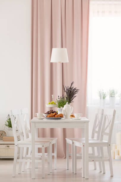 istock White chairs at table with flowers under lamp in dining room interior with pink drapes. Real photo 1048784304