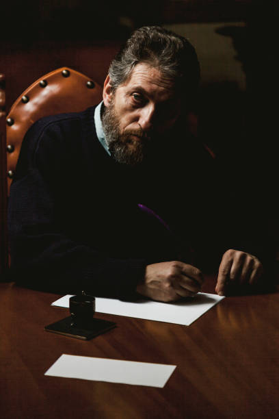 istock writer with beard writes on white sheet with goose feather 1048784728