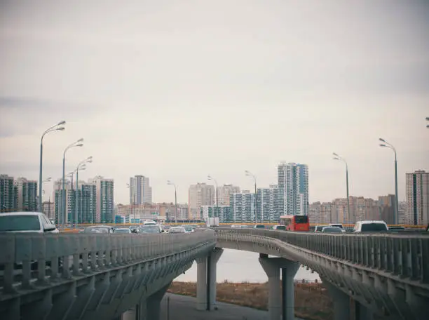 Cars go on bridge-roads on the background of the daytime overcast city. Wide shot