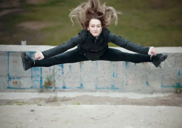 Girl jumping doing splits on the street against the background of a wall with graffiti. Wide shot