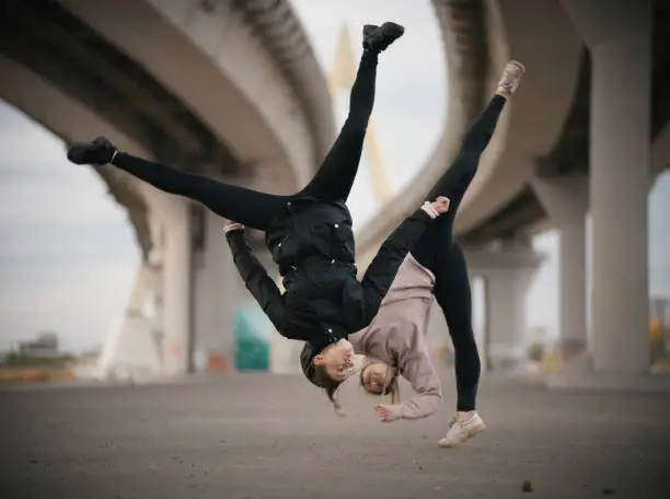 Girls perform splits in the air while jumping on the urban background of the bridge. Wide shot