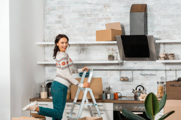 istock laughing young woman standing on ladder in kitchen with cardboard boxes during relocation at new home 1048800146