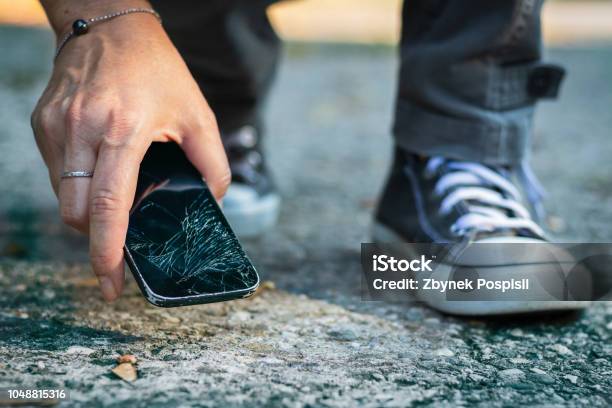 Woman Picking Up Broken Smartphone From The Ground Stock Photo - Download Image Now