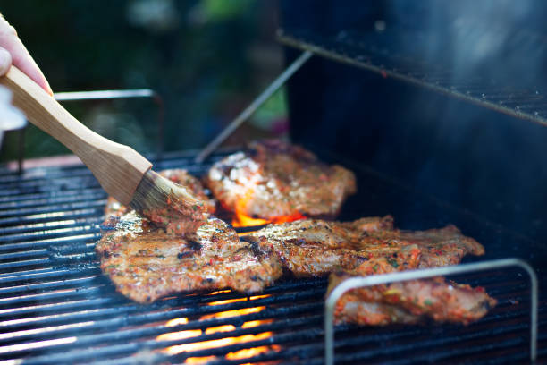 marinar la carne durante el asado a la parilla. cerdo a la parrilla. barbacoa en el jardín. - marinated fotografías e imágenes de stock