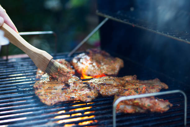 Marinating meat during grilling. Pork on the grill. Barbecue in the garden. Hand with a brush in motion. marinated photos stock pictures, royalty-free photos & images