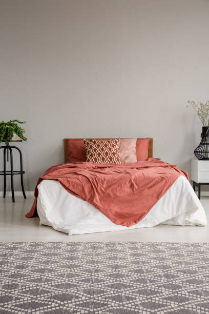 istock Patterned carpet in grey bedroom interior with red sheets on bed between plants. Real photo 1048821634