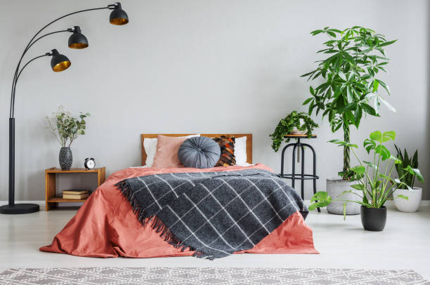 istock Red bed with patterned blanket between lamp and plants in grey bedroom interior. Real photo 1048821652