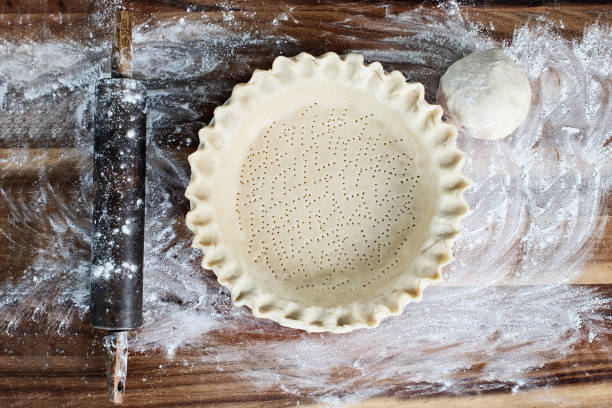 Homemade Butter Pie Crust in Pie Plate Homemade butter pie crust in pie plate with fluted pinched edge, rolling pin and extra ball of dough over floured rustic wooden background. Crust has been perforated with fork and ready for baking. sweet pie stock pictures, royalty-free photos & images