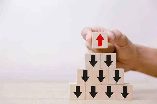 Hand putting wood cube block on top pyramid wooden blocks with red arrows facing opposite to the black arrows. With different concepts to other people. Going for success.