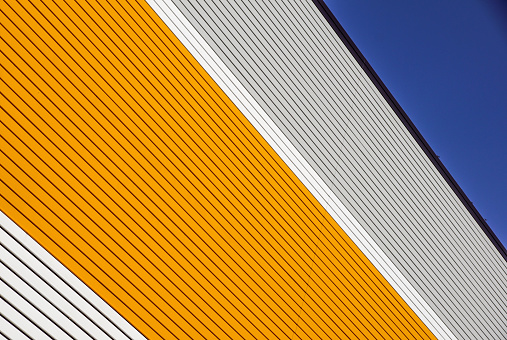 orange and white metal panel construction, wall of building with blue sky .