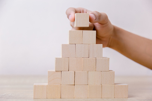 Hand putting wood cube block on top pyramid,With the concept of a thriving business going for success.