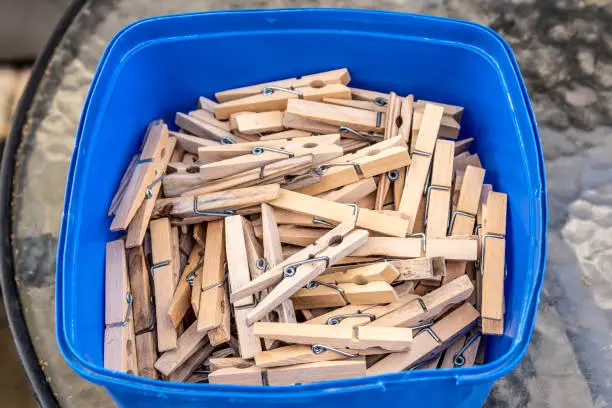 Many wooden clothes pegs in a blue plastic container