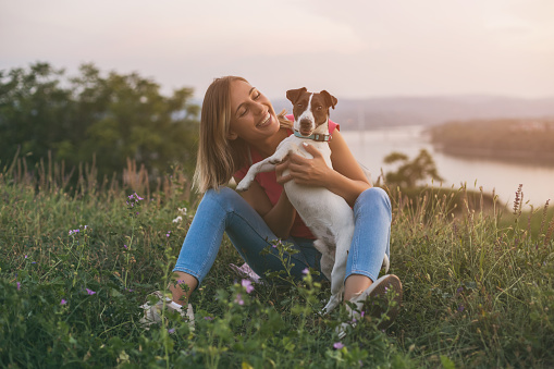 Beautiful woman enjoys spending time with her dog Jack Russell Terrier outdoor with a cityscape and river view behind her.Image is intentionally toned.
