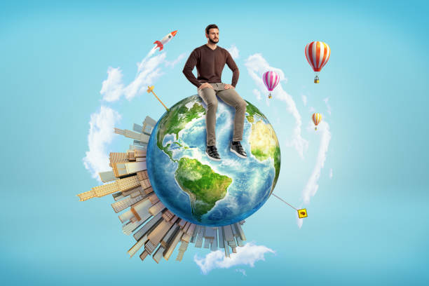 A bearded man sits on a small Earth globe with skyscrapers on its surface and hot air balloons flying around. A bearded man sits on a small Earth globe with skyscrapers on its surface and hot air balloons flying around. Man and Earth. Ecology or business. Open world for achievement. Elements of this image are furnished by NASA better world stock pictures, royalty-free photos & images