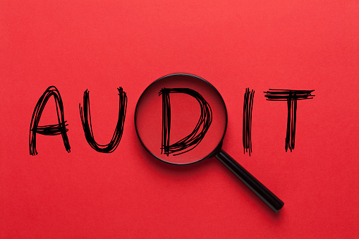 AUDIT written on red background and magnifying glass. Business concept.