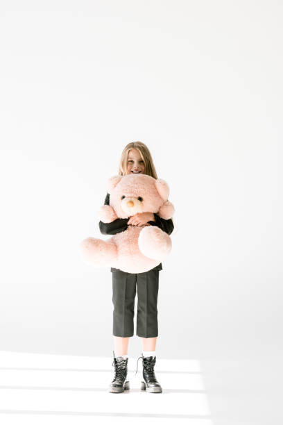 istock stylish cheerful kid in black suit holding big soft teddy bear on grey 1048894870
