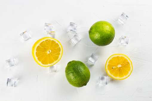 Fresh lime and lemon on white texture surface with crystal ice cubes. Close up.