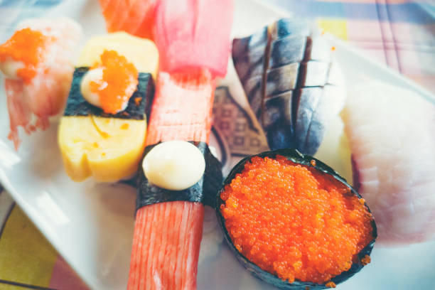Close-up sushi and sashimi mixed on wooden plate on black wooden table. Japanese food.