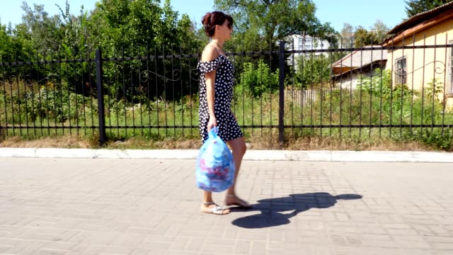 A beautiful girl in sunglasses is carrying a package of garbage in her hands, throwing out trash. summer hot day. ecology. separation of debris, cleanliness of the environment