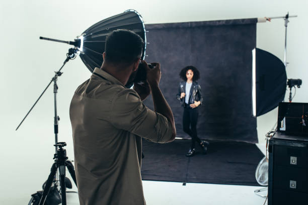 Photographer doing a photo shoot in a studio Model posing for a photograph during a photo shoot. Studio shot of a photographer shooting photos of a woman with studio flash lights on. photo studio model stock pictures, royalty-free photos & images