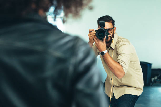 Photographer shooting photographs of a model in a studio. Rear view of a model posing for photograph during a photo shoot.