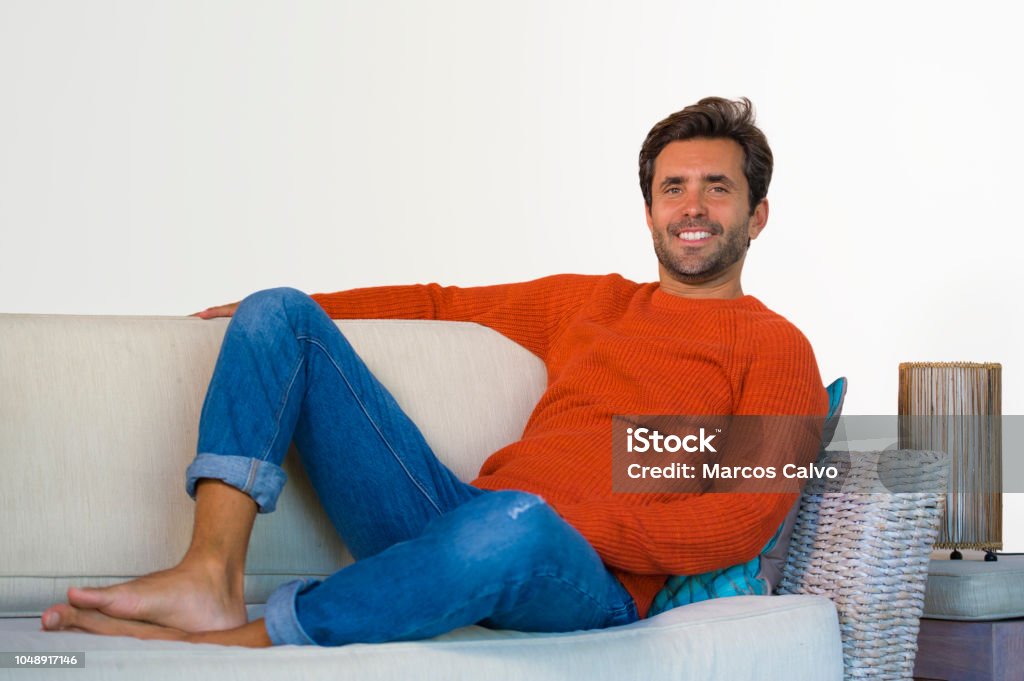 lifestyle home portrait of young attractive and happy 30s man smiling relaxed and comfortable sitting at living room sofa couch in his modern apartment cheerful and positive in success concept 30-39 Years Stock Photo