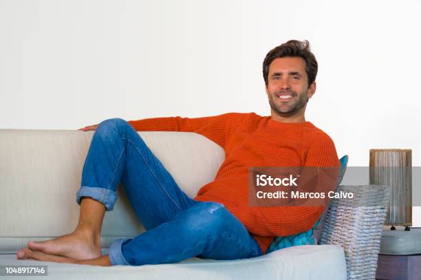 Lifestyle Home Portrait Of Young Attractive And Happy 30s Man Smiling Relaxed And Comfortable Sitting At Living Room Sofa Couch In His Modern Apartment Cheerful And Positive In Success Concept Stock Photo - Download Image Now