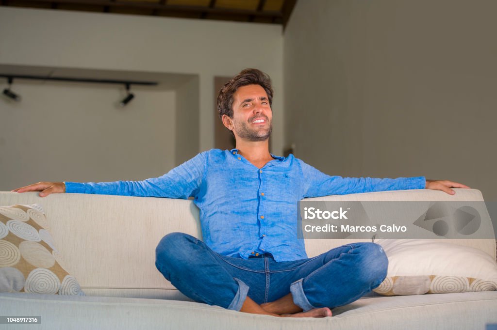 lifestyle home portrait of young attractive and happy 30s man smiling relaxed and comfortable sitting at living room sofa couch in his modern apartment cheerful and positive in success concept 30-39 Years Stock Photo