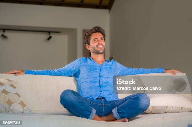 Lifestyle Home Portrait Of Young Attractive And Happy 30s Man Smiling Relaxed And Comfortable Sitting At Living Room Sofa Couch In His Modern Apartment Cheerful And Positive In Success Concept Stock Photo - Download Image Now