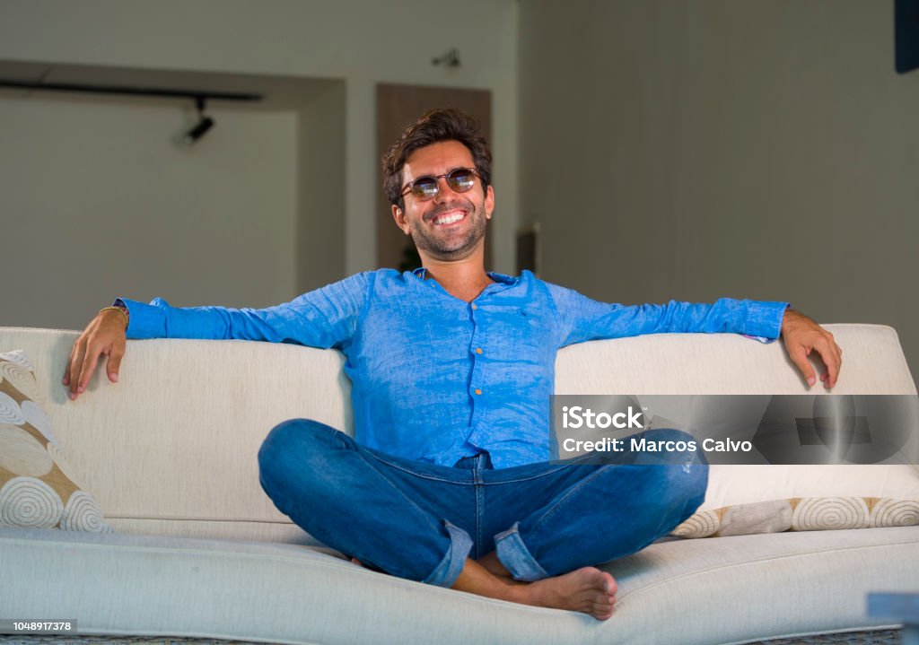 lifestyle home portrait of young attractive and happy 30s man smiling relaxed and comfortable sitting at living room sofa couch in his modern apartment cheerful and positive in success concept 30-39 Years Stock Photo