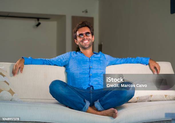 Lifestyle Home Portrait Of Young Attractive And Happy 30s Man Smiling Relaxed And Comfortable Sitting At Living Room Sofa Couch In His Modern Apartment Cheerful And Positive In Success Concept Stock Photo - Download Image Now