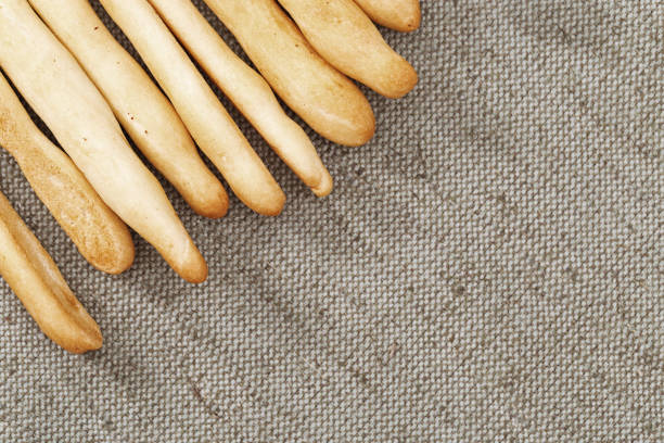 Italian grissini dry breadsticks close up on grey colored tablecloth. Food background with copy space. Grissini on fabric texture surface. Toned image.