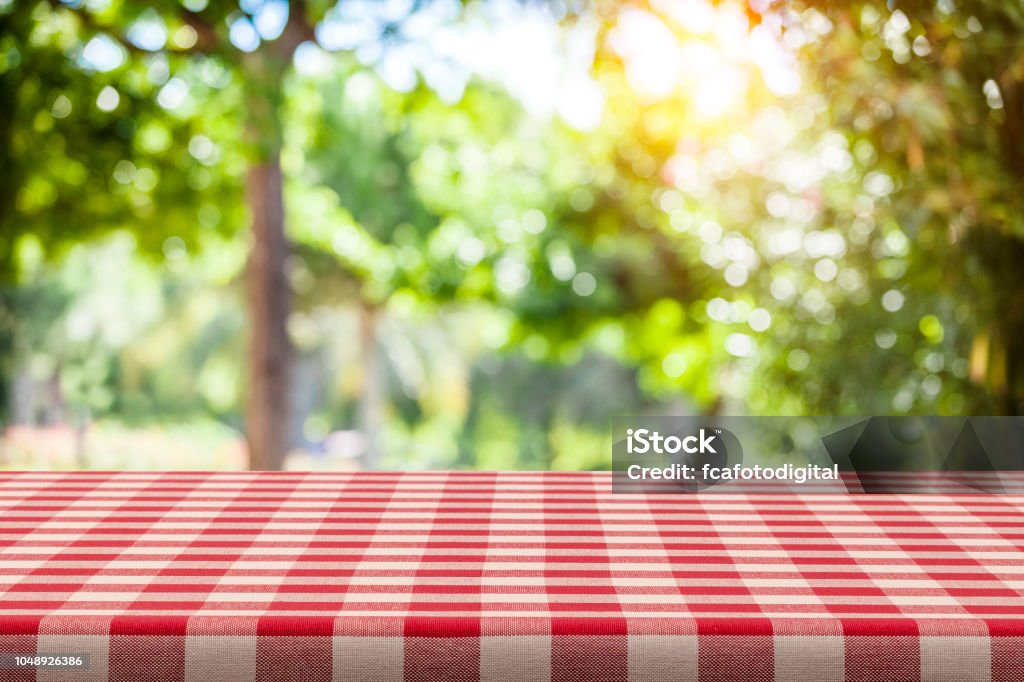 Backgrounds: Red and white checkered tablecloth with green lush foliage at background Empty table covered with red and white checkered tablecloth with defocused lush foliage at background. Ideal for product display on top of the table. Predominant color are green and red. DSRL studio photo taken with Canon EOS 5D Mk II and Canon EF 100mm f/2.8L Macro IS USM. Picnic Stock Photo
