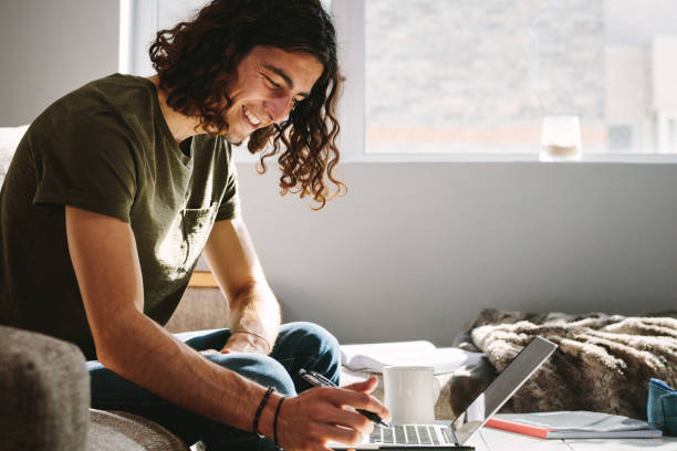 istock Smiling man studying at home on laptop with a pen in hand 1048931514