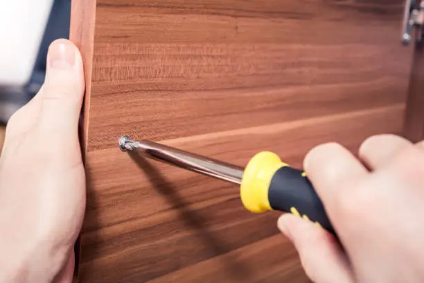 Loosening The Screw Of A Doorhandle Of A Brown Cupboard With Screwdriver, DIY Concept