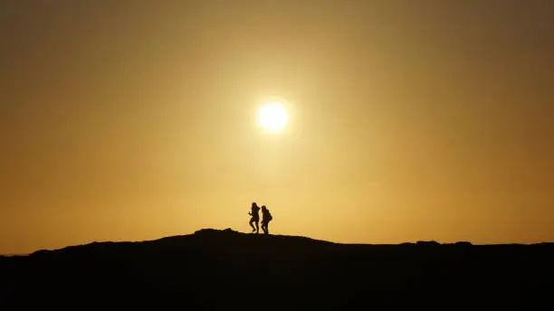 A silhouette shot of a young couple climbing and exploring a hillside in Donegal, Ireland against a golden sunset sky.
