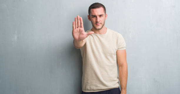 istock Young caucasian man over grey grunge wall with open hand doing stop sign with serious and confident expression, defense gesture 1048946078