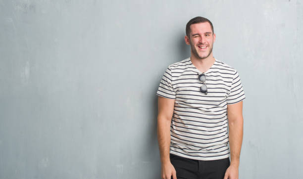 istock Young caucasian man over grey grunge wall winking looking at the camera with sexy expression, cheerful and happy face. 1048946316